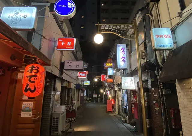A narrow Golden Gai lane at night lined with small lit bar signs and a red lantern