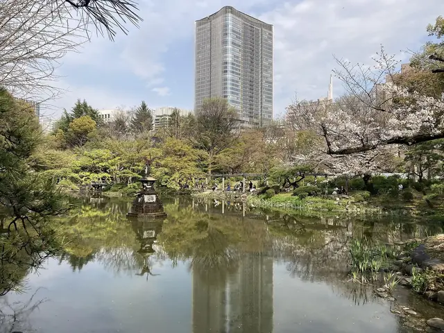 A garden pond in Hibiya Park framed by pines and cherry blossoms, with a tower behind