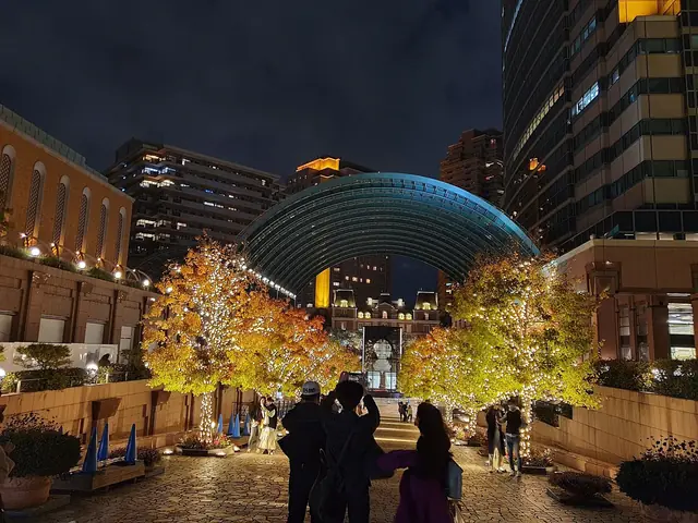 Lit trees leading to the glass arcade of Ebisu Garden Place at night