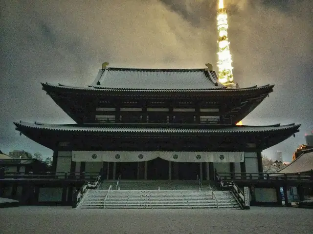 雪の夜の増上寺大殿と背後に輝く東京タワー